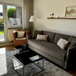 Wohnzimmer mit bequemen Schlafsofa und Blick auf die Terrasse und den angrenzenden Garten.