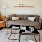 Wohnzimmer mit Schlafsofa für zwei Personen. Links vom Sofa steht ein Lesesessel mit Stehleuchte. Vor dem Sofa stehen zwei kleine Beistelltische.