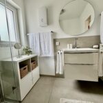 Modernes Badezimmer mit beleuchtetem Wandspiegel über dem Waschbecken und zusätzlichem Schminkspiegel – ideal für die tägliche Pflege.